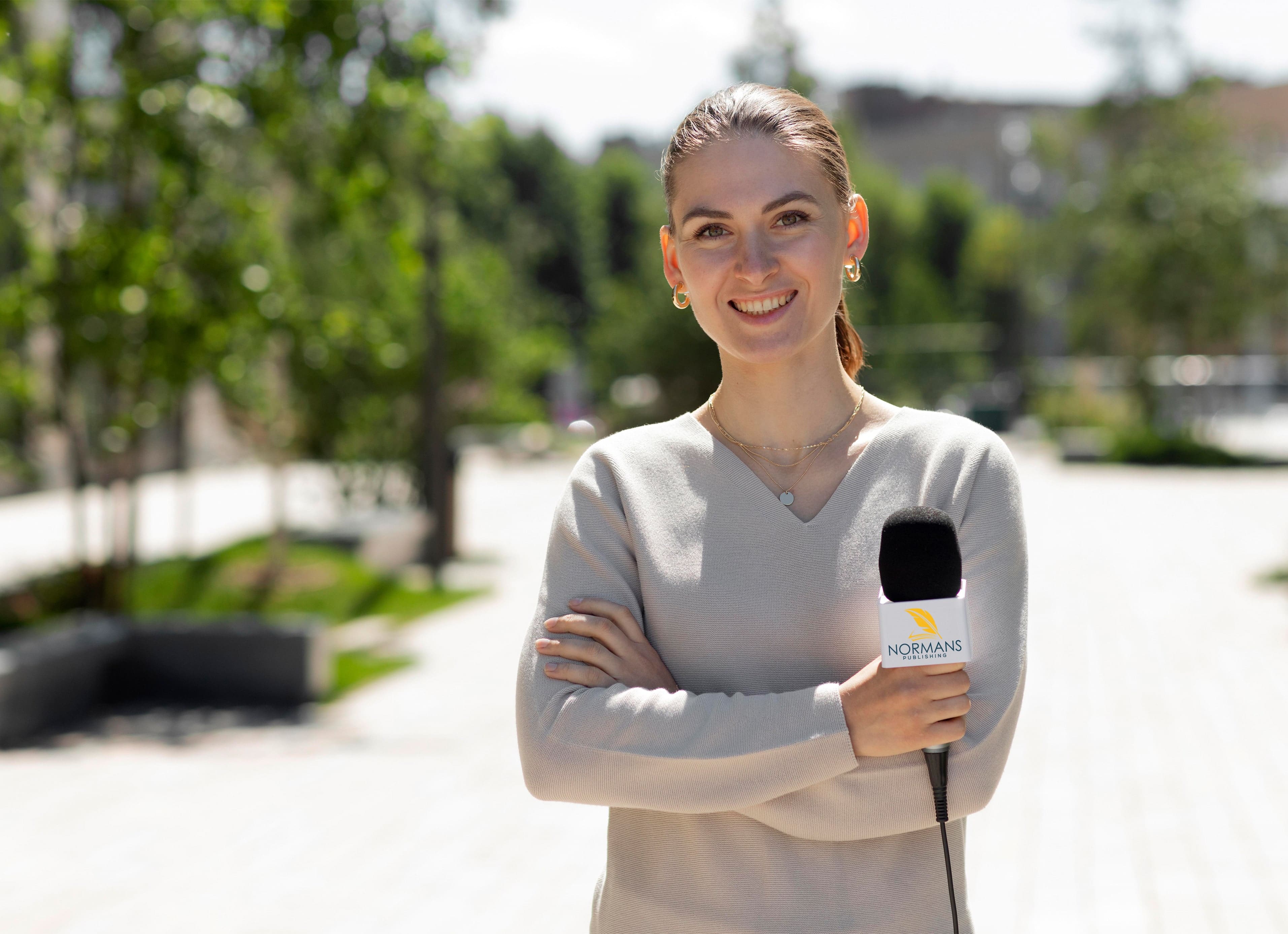 A woman confidently holds a microphone, standing in front of a majestic building.